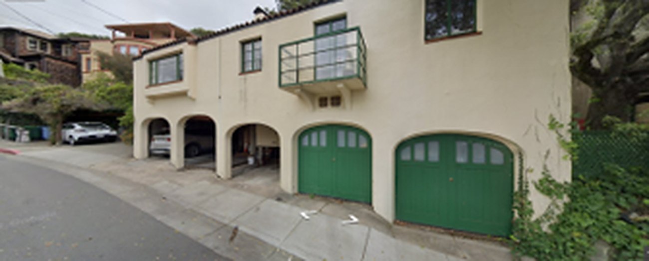 A pale stucco house above a row of arched bays and two green garage doors