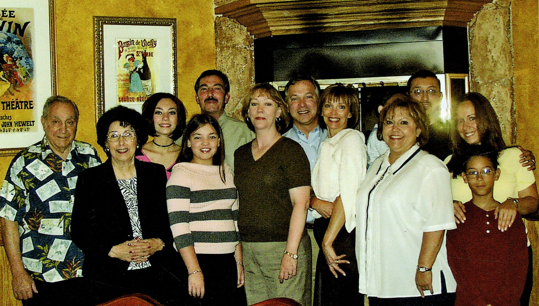 Twelve members of the Benedetto family gathered together indoors, framed posters on a gold wall behind them