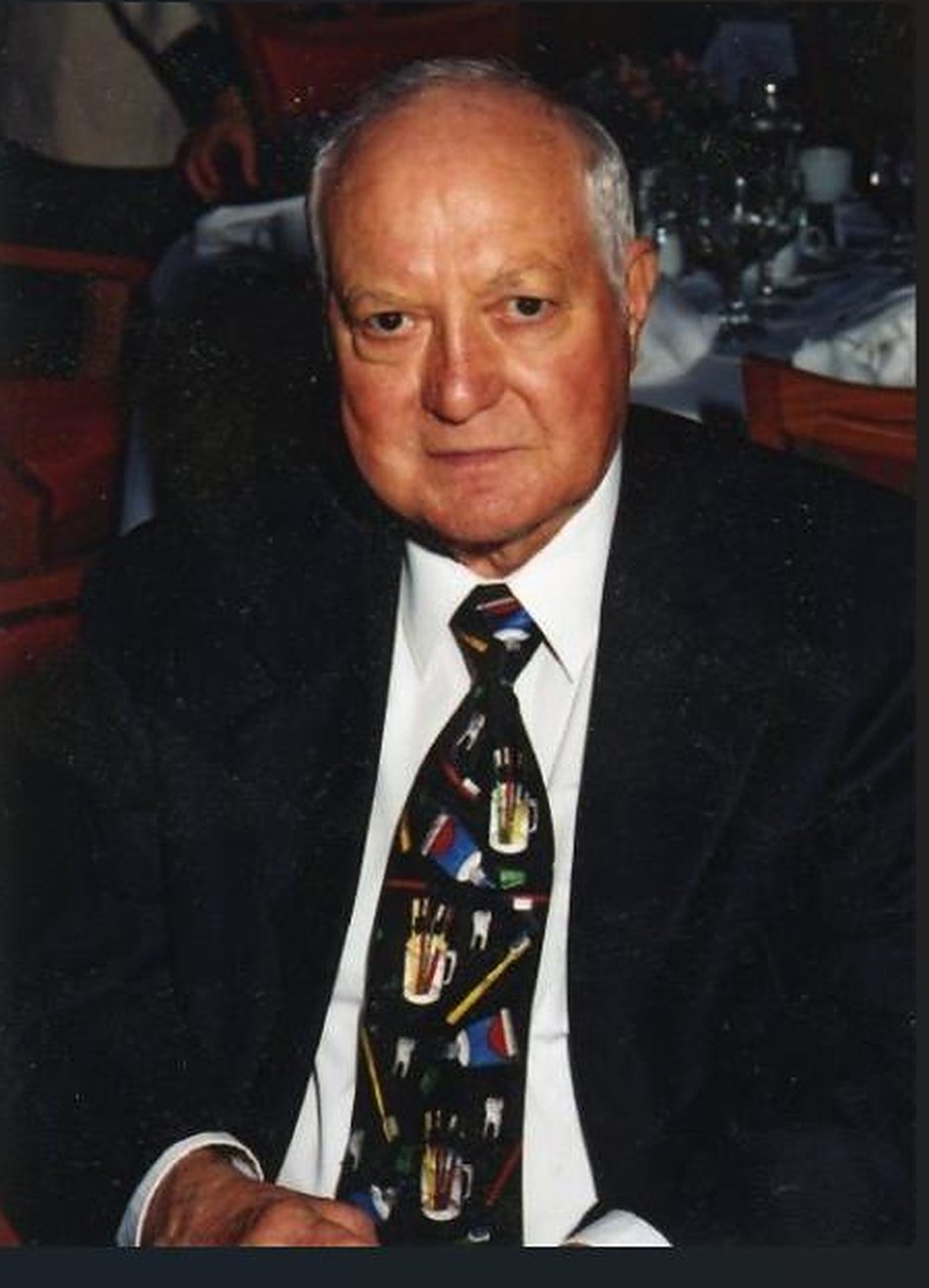 Benedict F. Enea in a dark suit and patterned tie, seated at a table