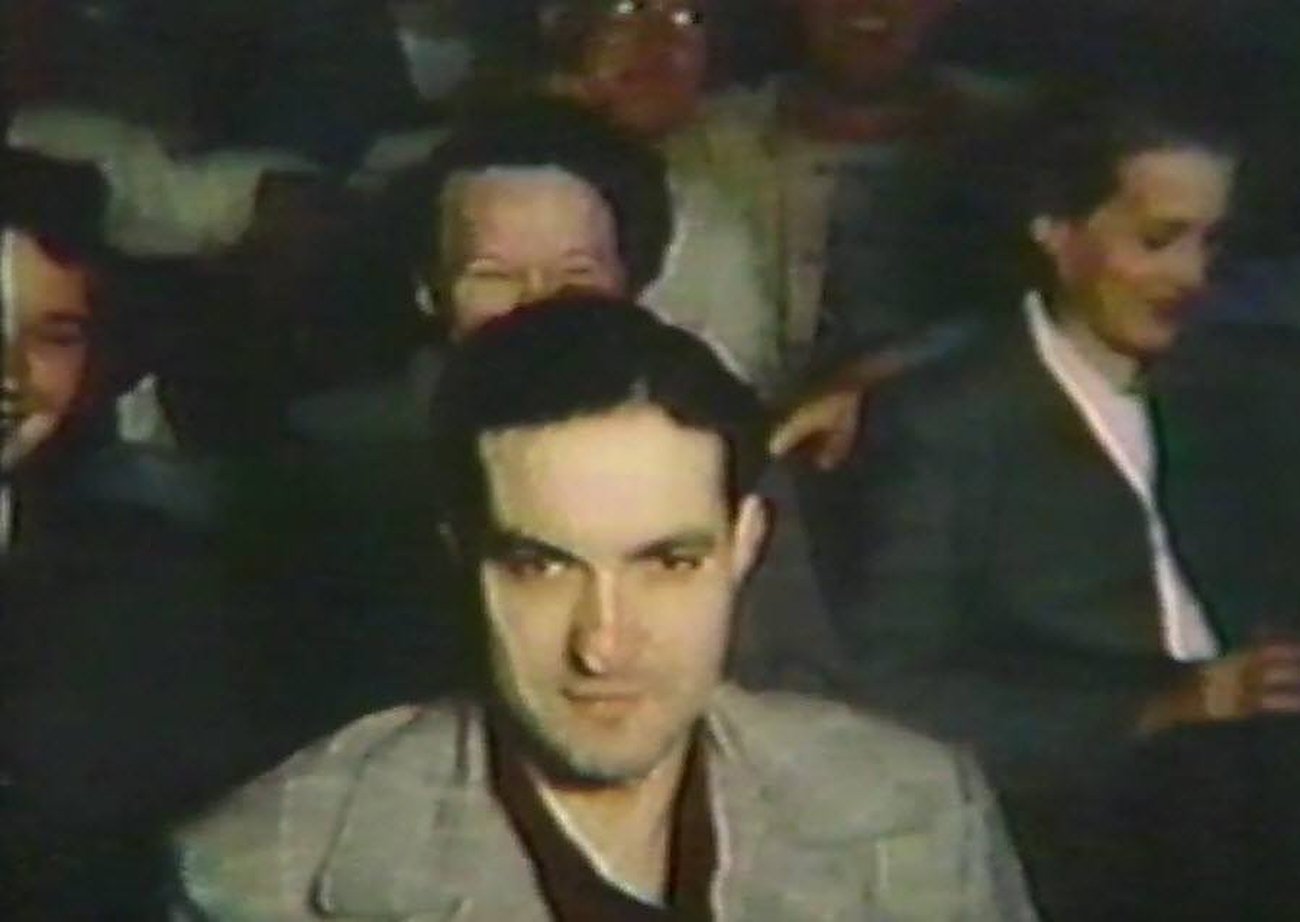 A film frame showing Benny Enea seated among an audience in a cinema