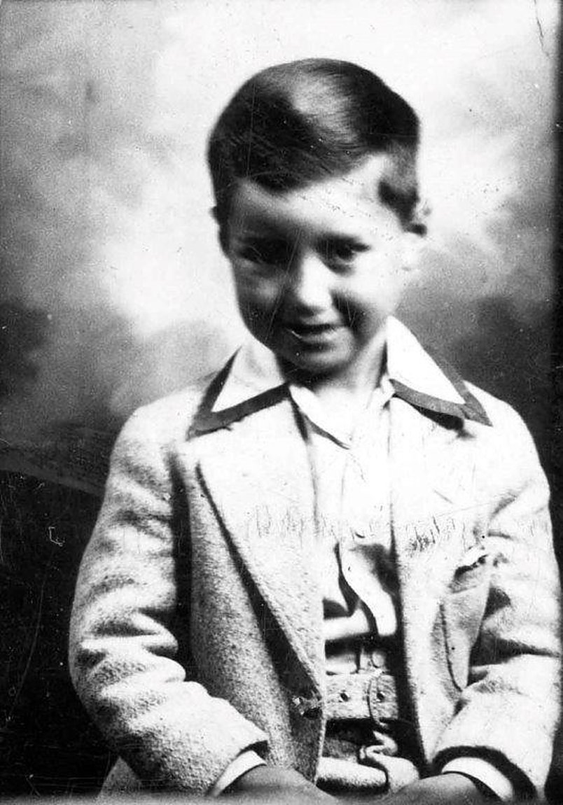 Studio portrait of a boy in a light tweed jacket, looking down and smiling
