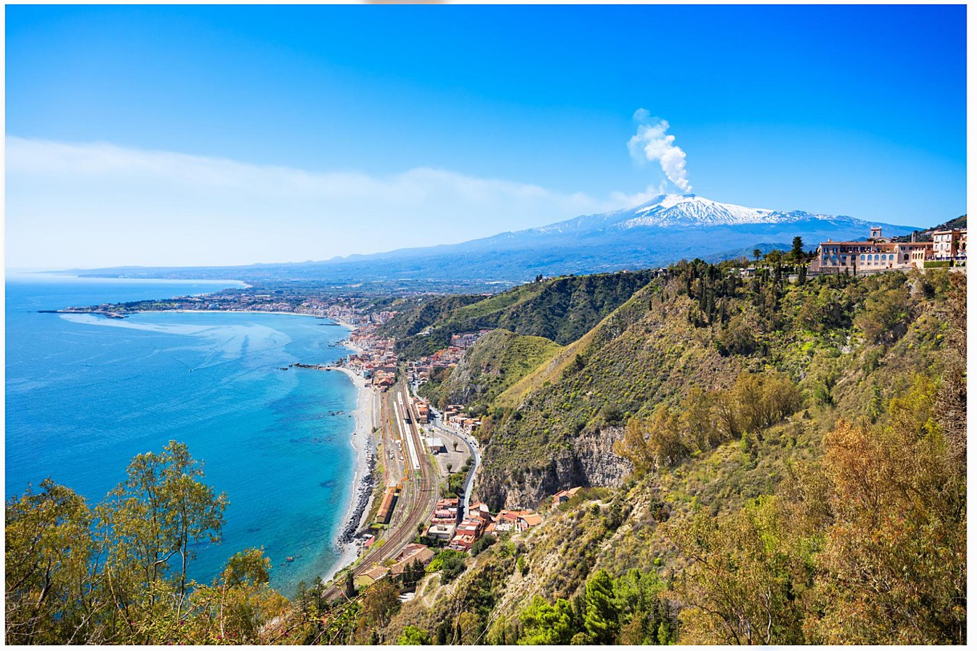 Daytime panoramic view of the Sicilian coast with snow-capped Mount Etna in the distance