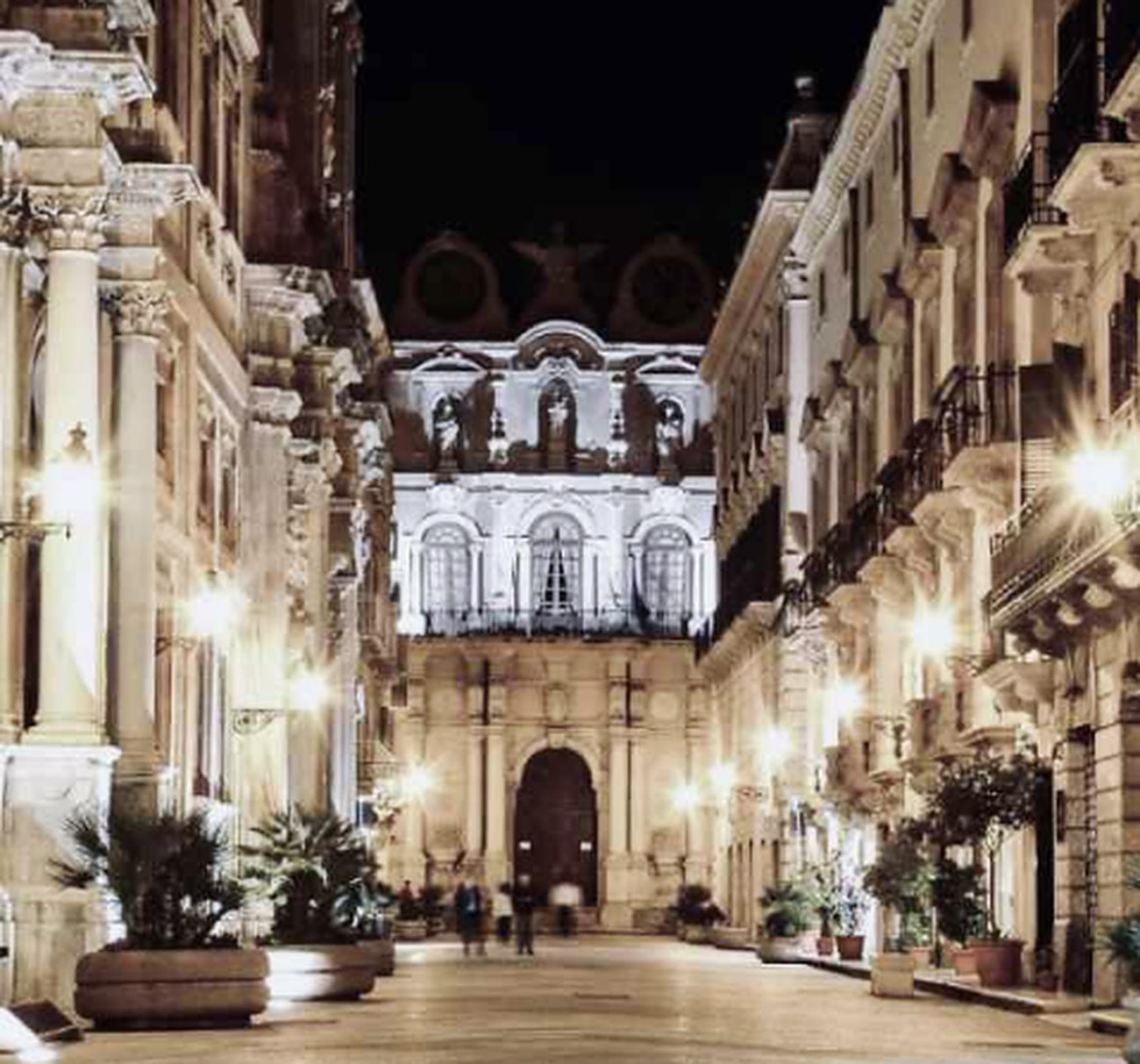 Corso Vittorio Emanuele in Trapani at night, lined with lamps and palms, the Palazzo Cavarretta at the far end