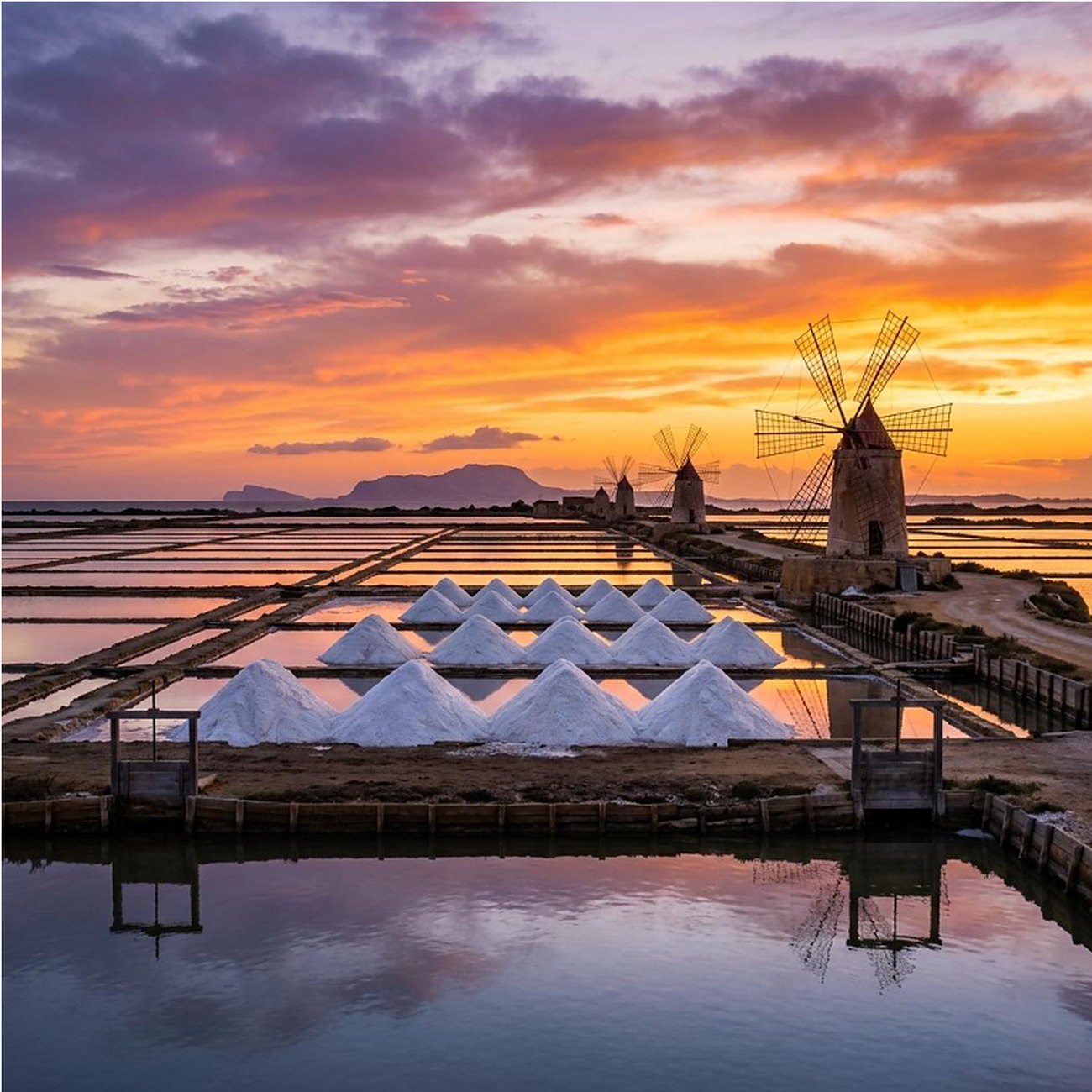 Trapani salt pans and windmills at sunset, with white salt mounds and reflections in the water