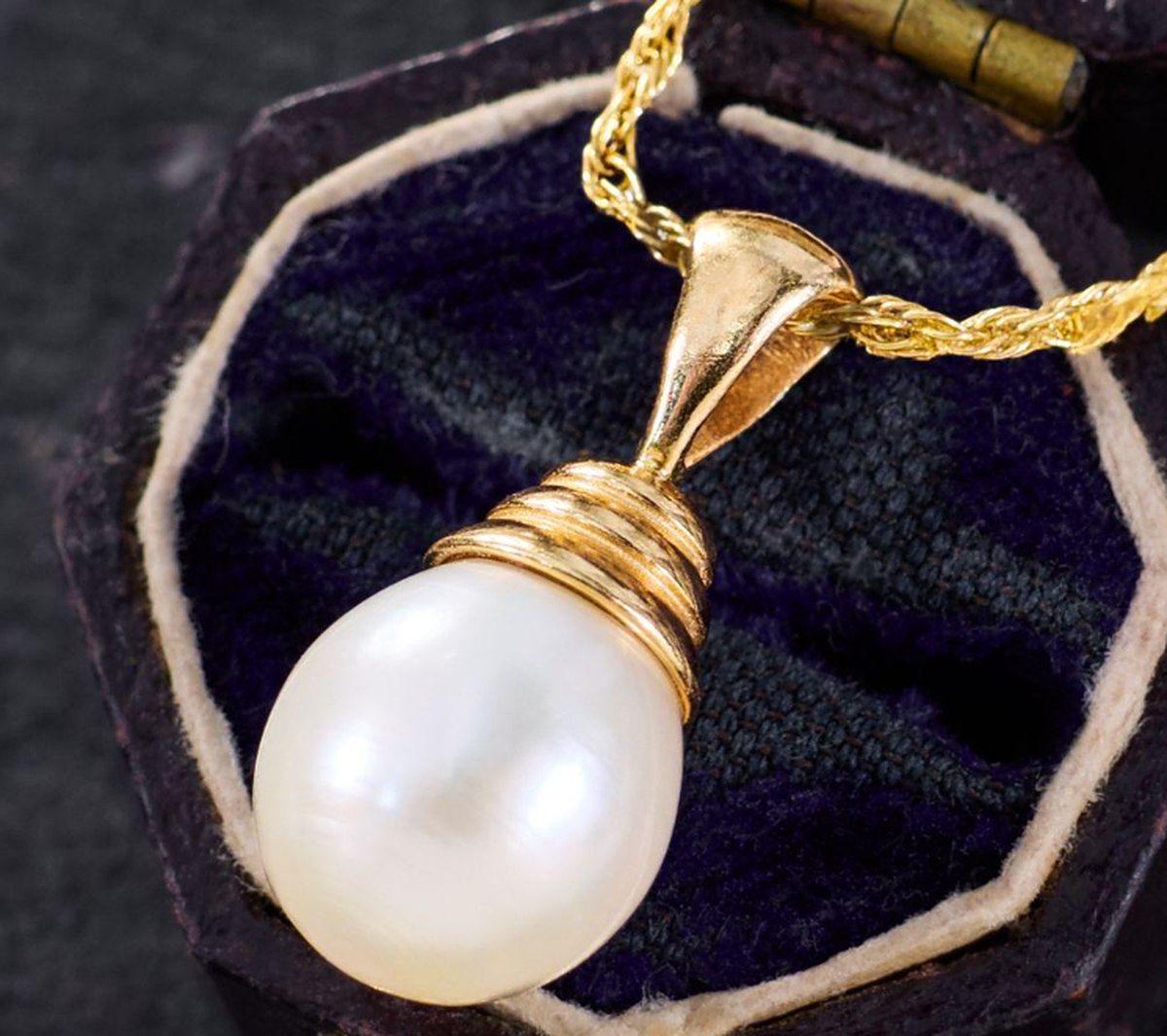 A pearl pendant on a gold setting, shown against a dark cloth