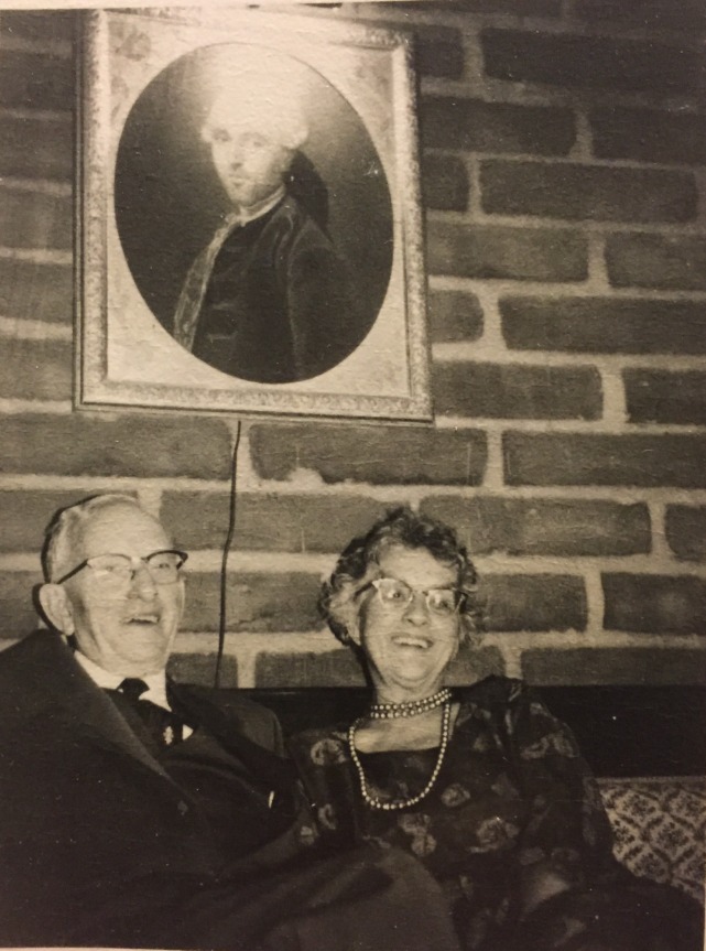 Charles and Florence Mel seated beneath an oval portrait of an eighteenth-century gentleman