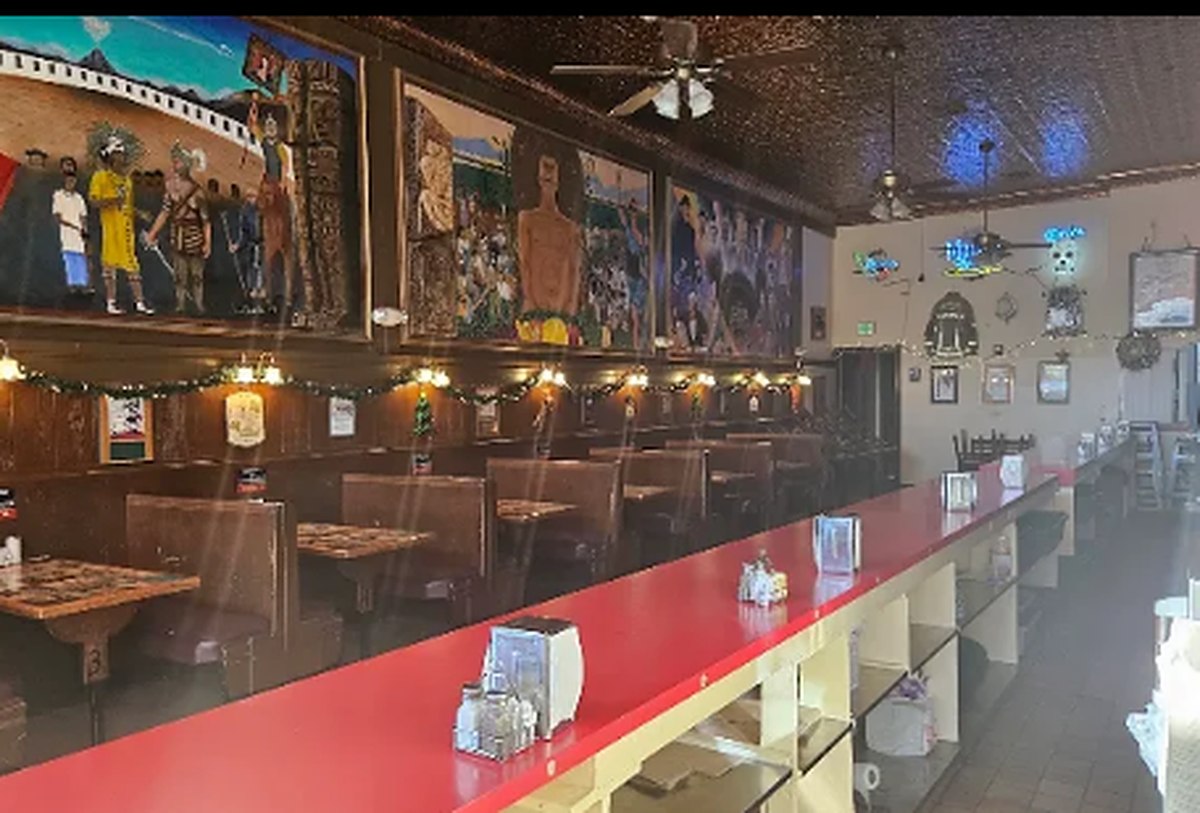 The dining room of the New Mecca Cafe, a long red counter and booths beneath a painted mural