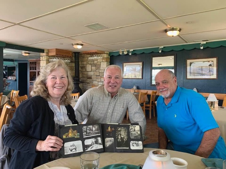 Barbara Stubbs holding open a family photo album beside Charles Enea and Michael Giambona Jr.