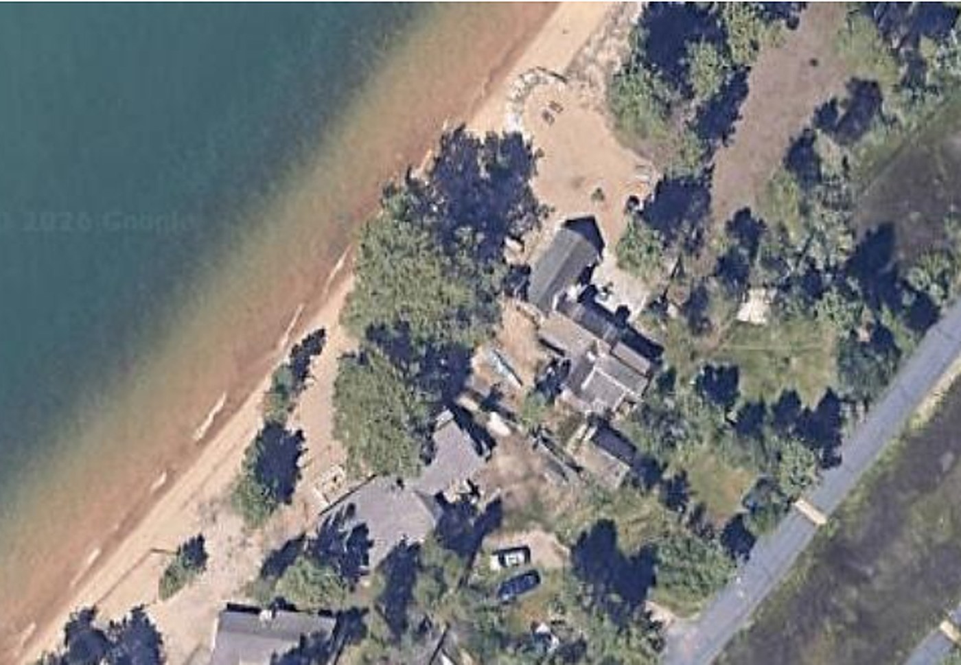 An aerial view of lakeside cabins among pines along a sandy shoreline