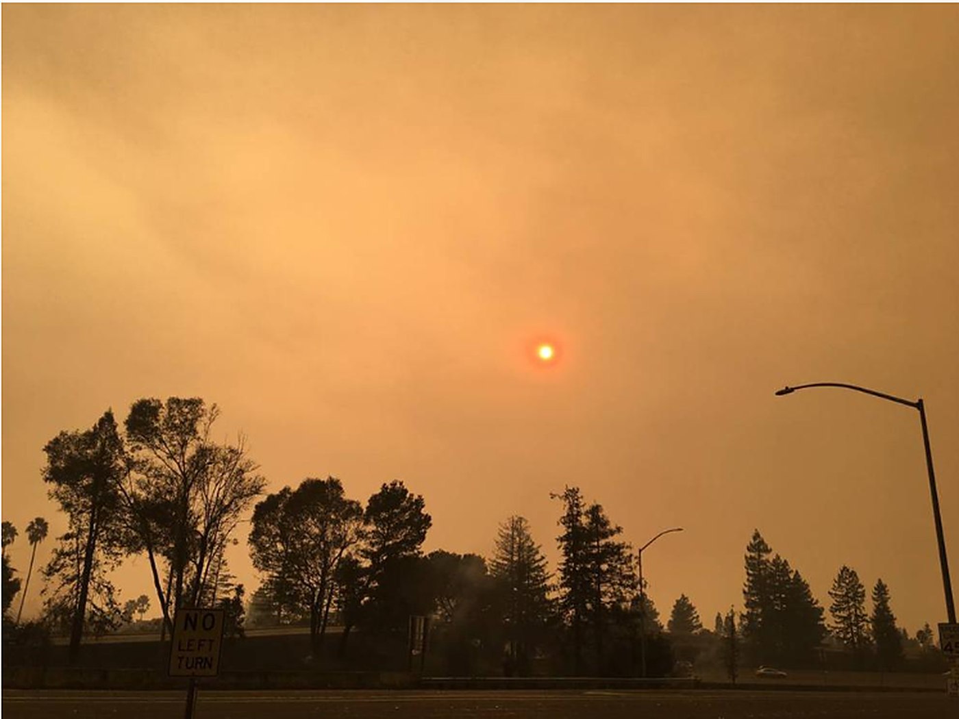 An orange sky thick with wildfire smoke, the sun a dim red disc above dark trees