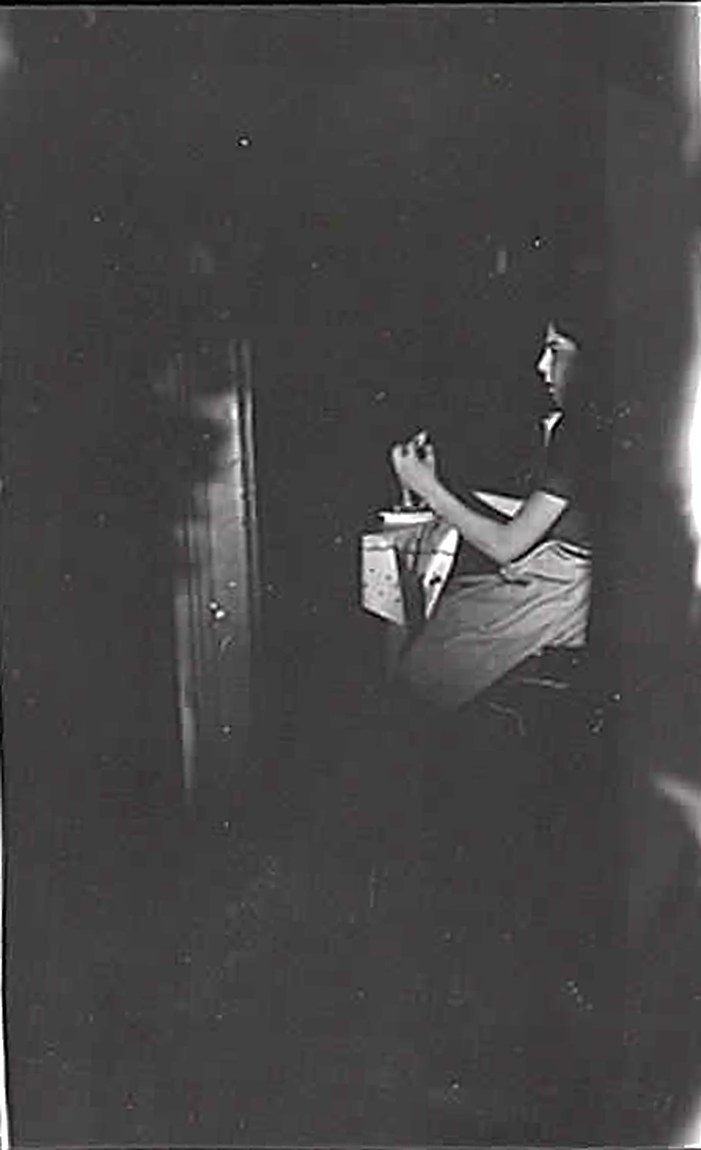 A dimly lit candid photograph of a young woman seated at a kitchen table