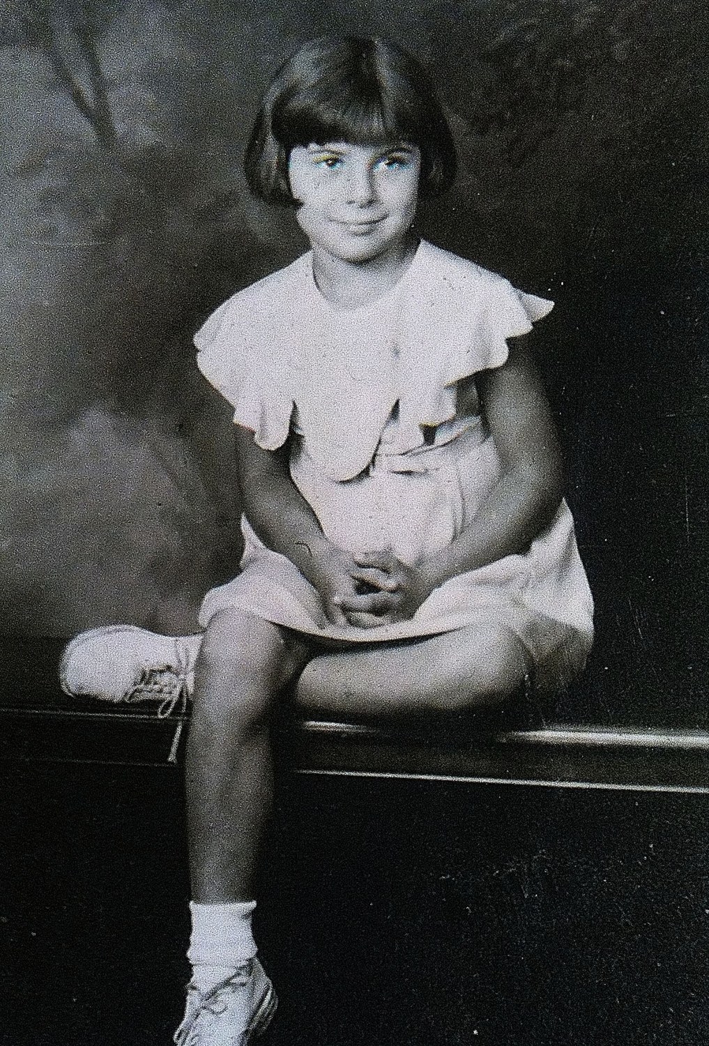 Studio portrait of a young girl with a bobbed haircut seated on a bench in a light dress