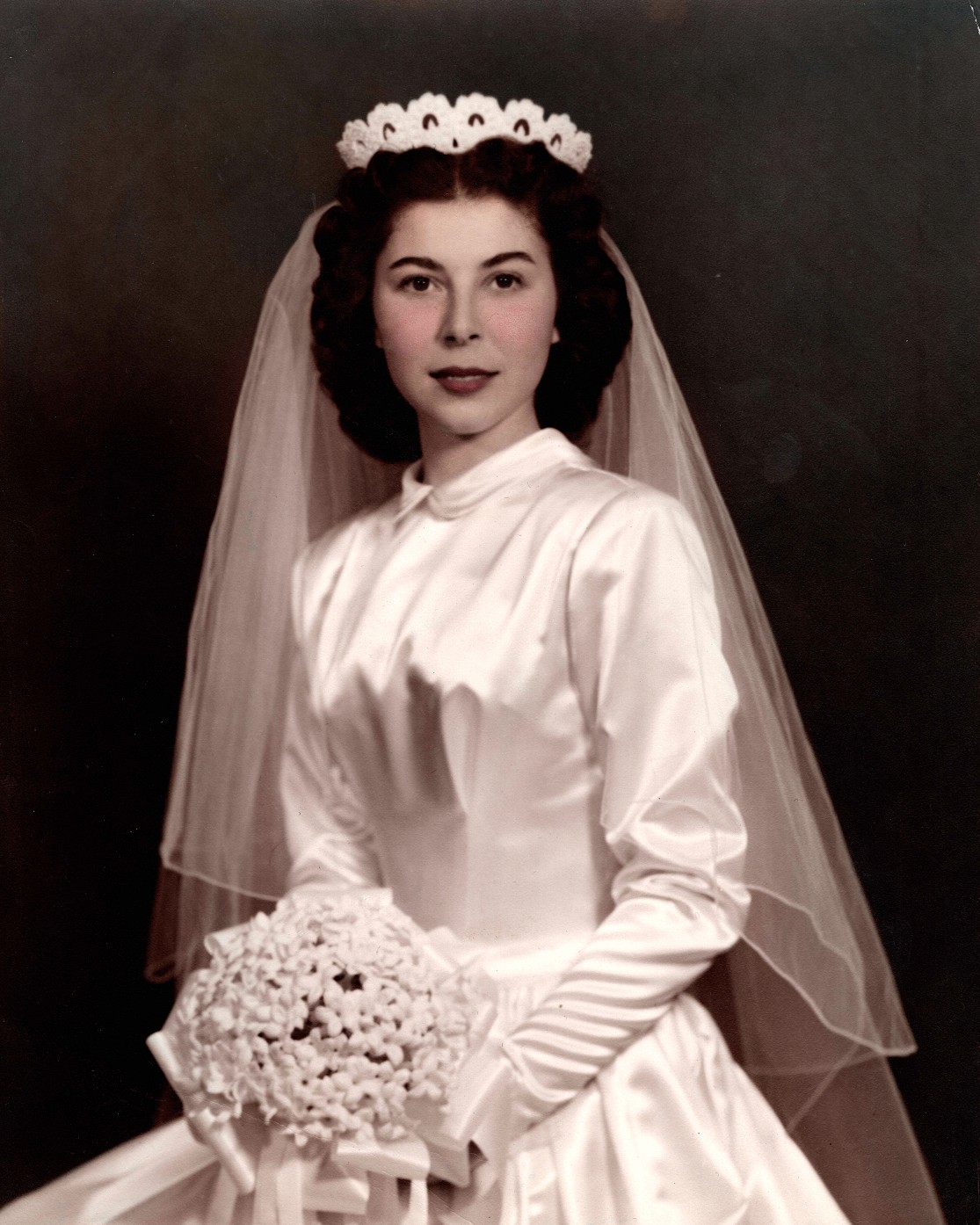 Hand-tinted wedding portrait of a bride in a satin gown and veil holding a bouquet