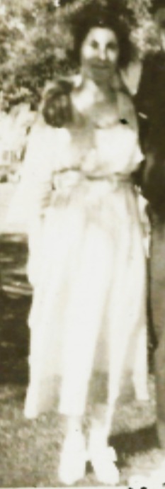 A standing portrait of a young woman in a light dress, photographed outdoors