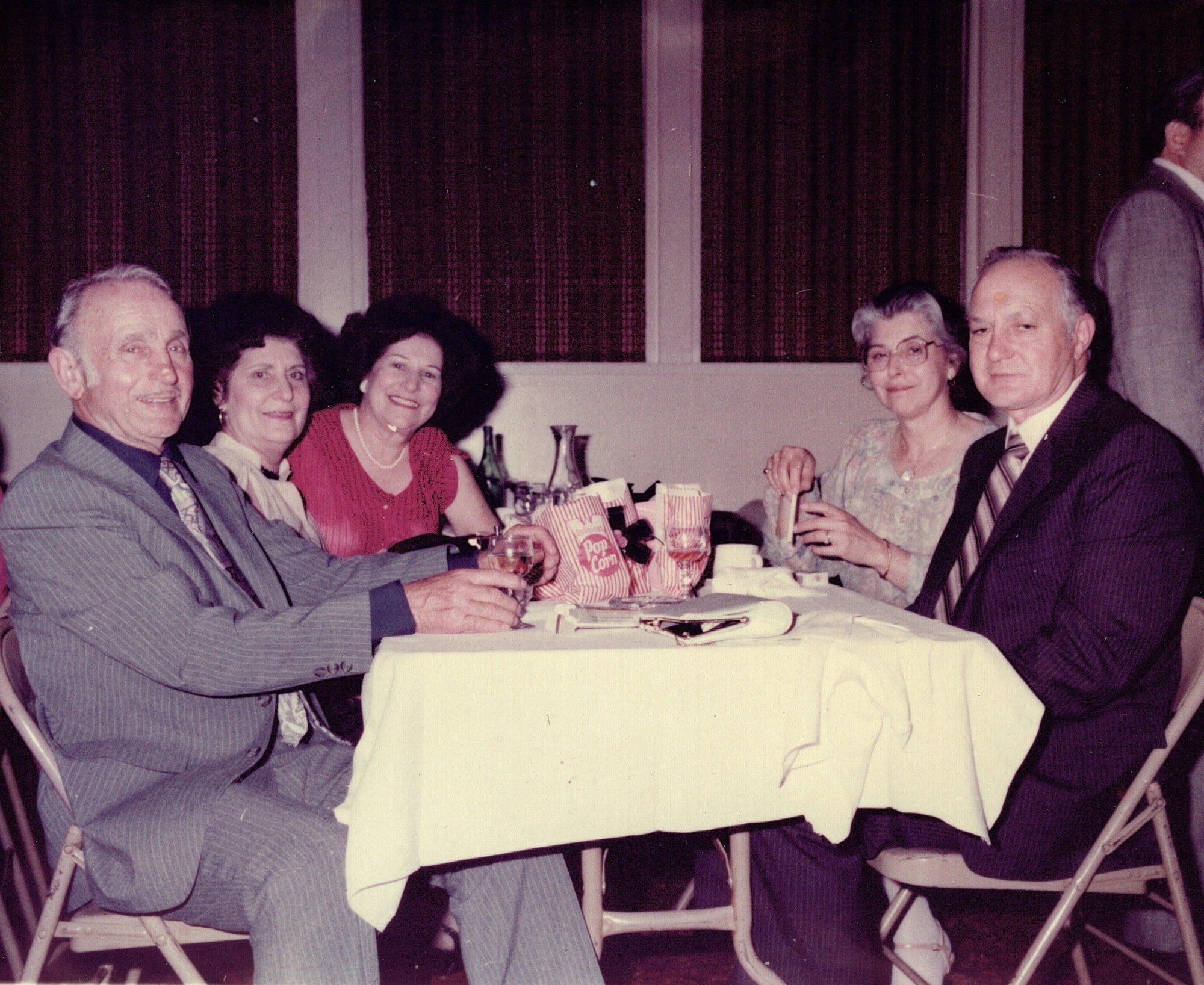 Five people seated around a cloth-covered table at a club dinner, raising glasses toward the camera