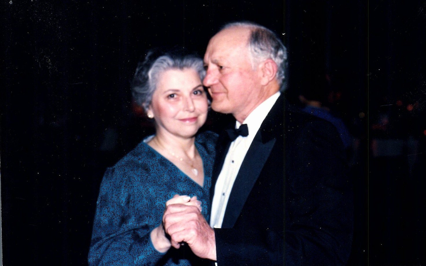 A couple dancing closely, the man in a tuxedo and the woman in a dark patterned dress