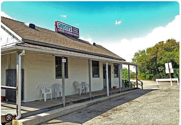The low white clapboard exterior of Giusti's Place with its roof sign and covered porch