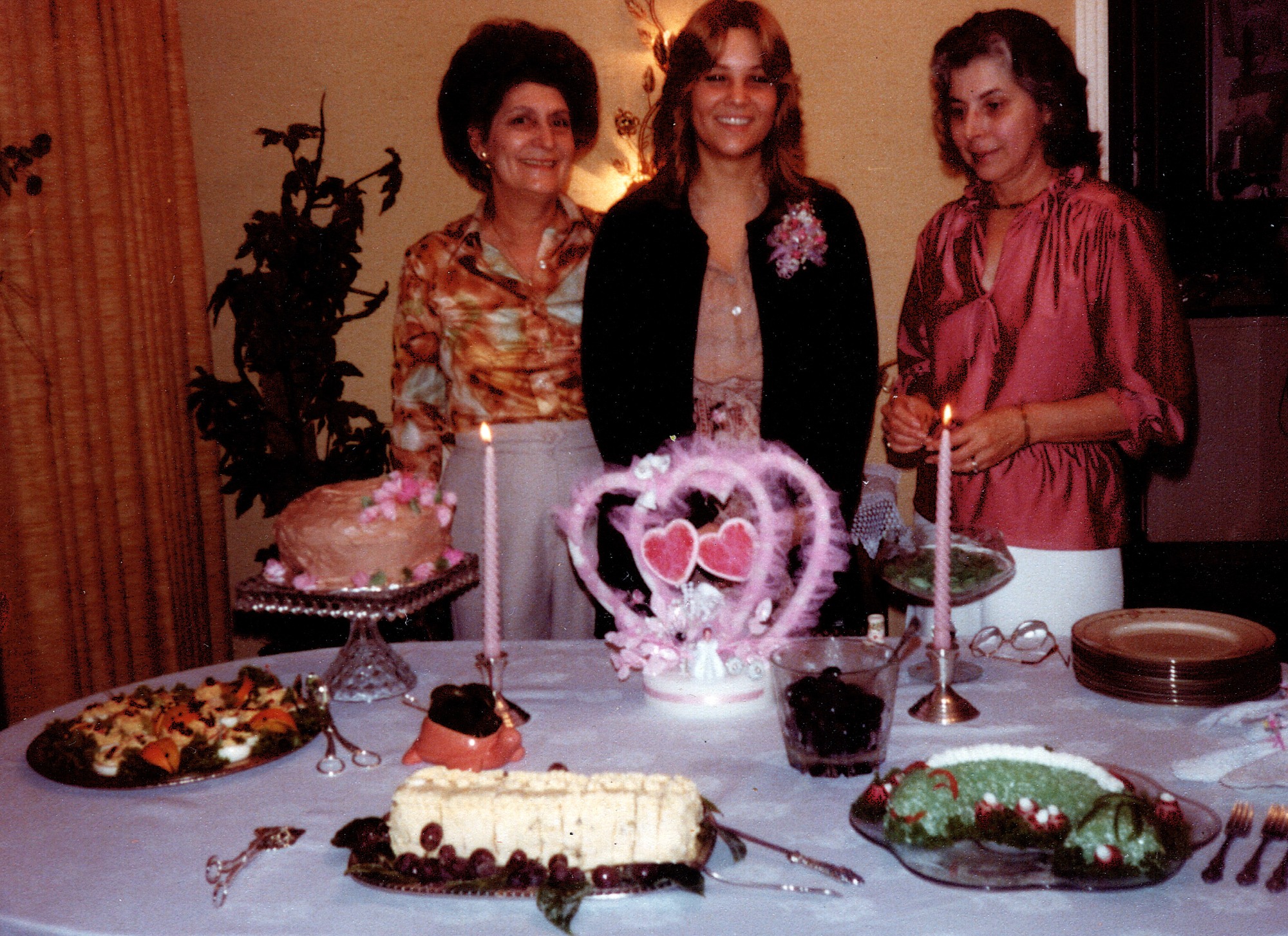 Three women standing behind a table laid with cakes and platters at a bridal shower