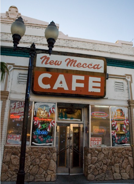 The storefront of the New Mecca Cafe beneath its painted sign and a street lamp