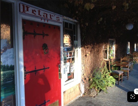 A red wrought-iron-strapped door beneath a Petar's Pub sign, beside an ivy-covered wall and an outdoor seating area