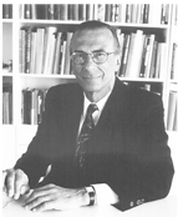 Portrait of Dr. George Solomon seated at a desk before a wall of books