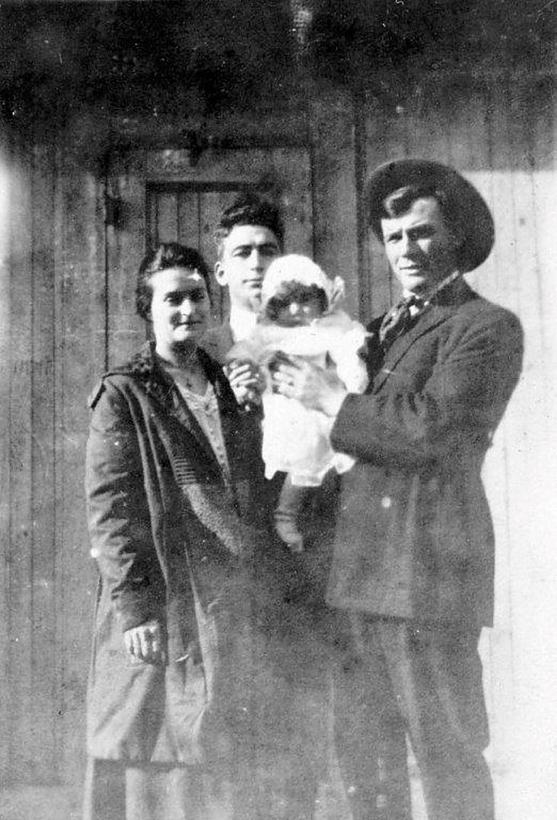 Three adults and an infant standing before a wooden door, Pittsburg, California, circa 1919