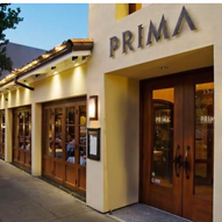 The exterior of Prima restaurant at dusk, warm light behind folding glass doors