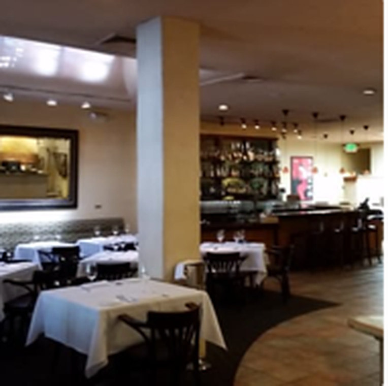 The dining room at Prima, white-clothed tables and a lit bar beyond