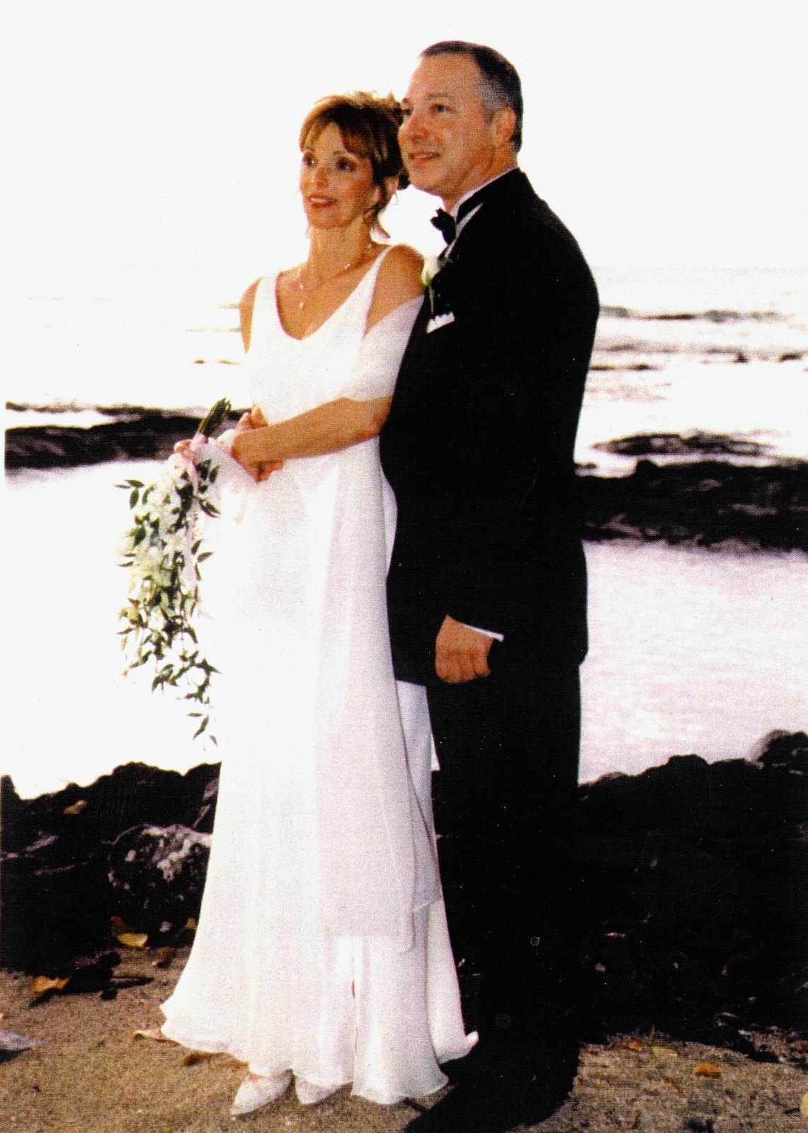 Tami and Charles Enea on their wedding day, standing on lava rock above the water at sunset